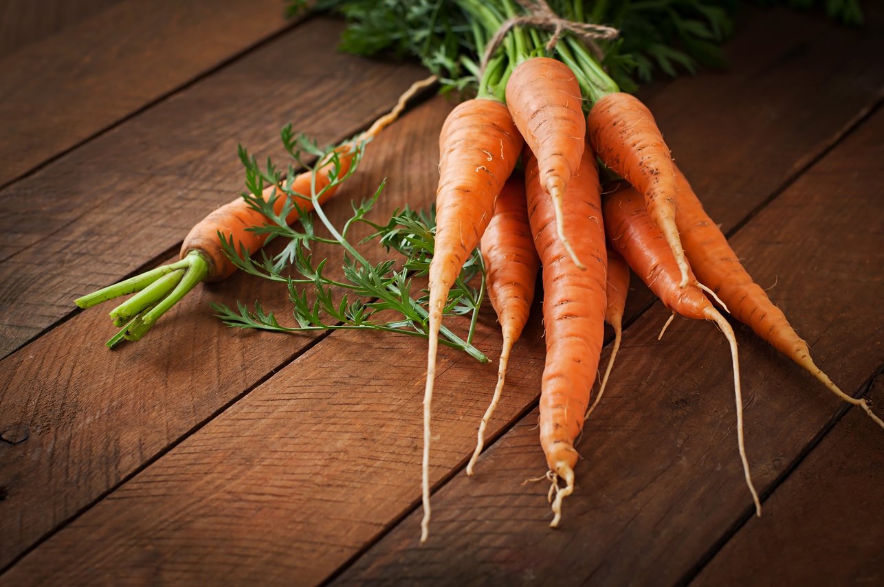 Bunch of fresh carrots with green leaves over wooden background