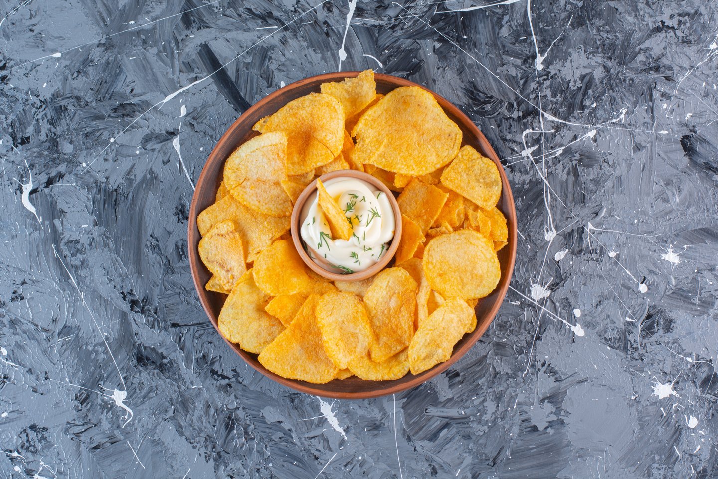 Yogurt and crispy potato chips in plate , on the marble background
